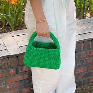 May include: A bright green knitted handbag with a top handle. The bag is small and has a rectangular shape.