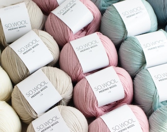 Könnte beinhalten: Eine Ansammlung von Merino-Wollknäueln in verschiedenen Pastellfarben, darunter Rosa, Beige und Türkis. Jedes Knäuel hat ein weißes Etikett mit dem Text "SO.WOOL MERINO WOOL". Die Wolle ist in einem ansprechenden Muster angeordnet.