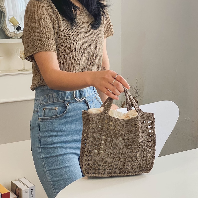May include: A brown crocheted tote bag with a white lining. The bag has a square shape and a woven design.