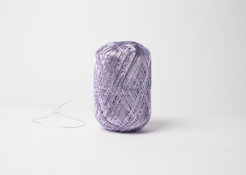 May include: A spool of lavender-colored yarn sits against a white background. The yarn is tightly wound, with a few loose strands extending from the main body. This yarn is suitable for various crafting projects.