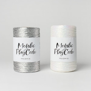 Op de afbeelding: Twee spoelen metallic garen, een zilveren en een witte, met de tekst "Metallic PlayCode" op elk etiket.