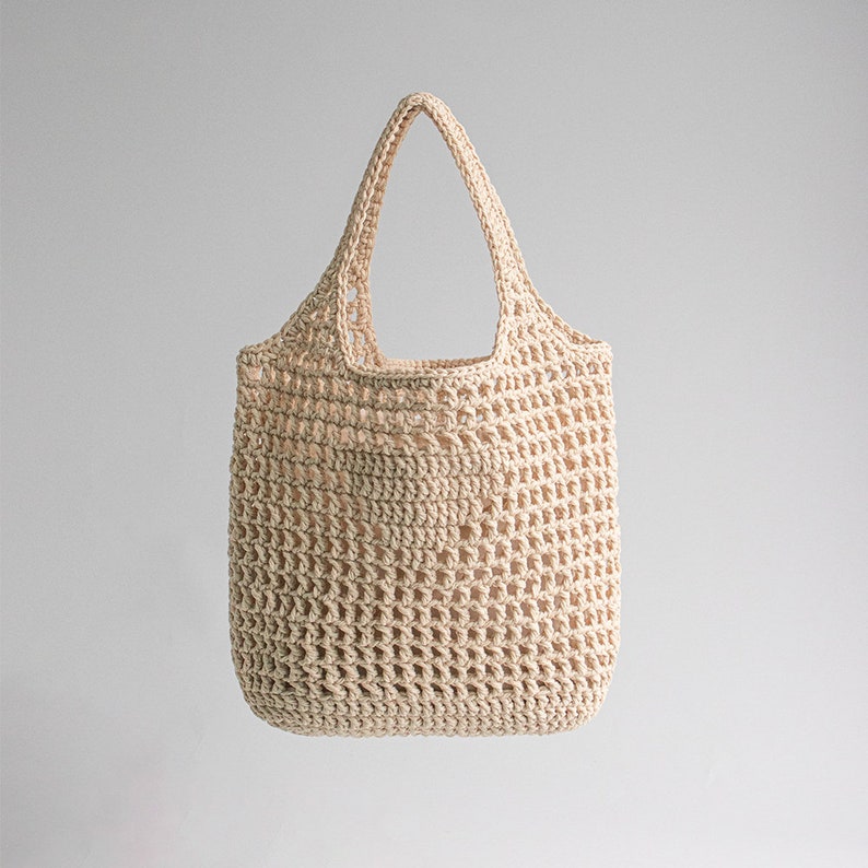 Puede incluir: Un bolso de mano de crochet beige con una parte superior ancha y abierta y dos asas.