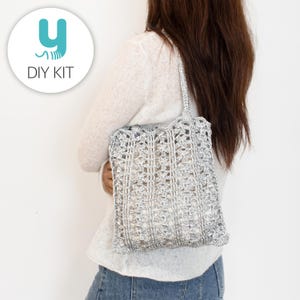 May include: A silver crocheted tote bag with a rectangular shape and a handle. The bag has an open weave design, allowing the contents to be partially visible. The text "DIY KIT" is in a white circle in the upper left corner.