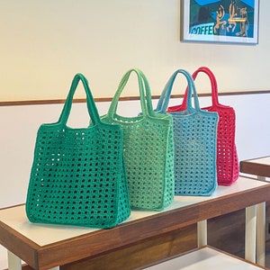 Puede incluir: Cuatro bolsas de mano de crochet en diferentes colores: verde, verde claro, azul y rojo. Las bolsas están hechas con un patrón de cuadrícula cuadrada y tienen una textura tejida.