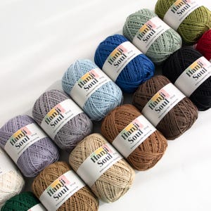 Puede incluir: Una colección de 12 carretes de hilo Hanji Soul en varios colores, incluyendo azul claro, marrón, beige, gris, verde y rojo. Cada carrete tiene una etiqueta con el texto "Hanji Soul" y las palabras "Willowbark Paper 100%" en una fuente más pequeña.