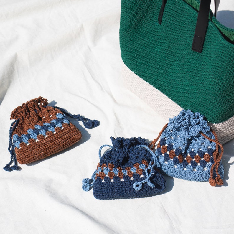 May include: Three crocheted drawstring bags with brown and blue geometric patterns. The bags are on a white fabric surface.