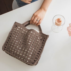 May include: A brown crocheted tote bag with a square grid pattern. The bag has two handles and is made of a lightweight material.