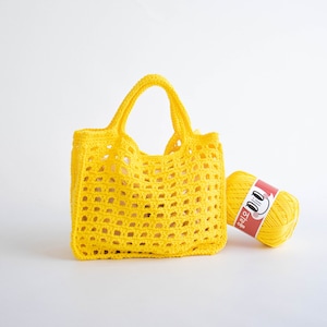 May include: A bright yellow crochet tote bag with a wide, open weave. The bag has a single handle and is sitting next to a ball of yellow yarn with a red label that says "D.I.Y.  TOTE"
