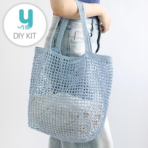 May include: A light blue crocheted tote bag with a net-like design. The bag has two handles and is being held by a person. The bag is filled with a white object. The image also includes a logo that says "DIY KIT".