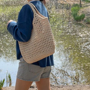 Puede incluir: Una persona con un su&eacute;ter azul y pantalones cortos de mezclilla lleva un bolso tote grande de crochet beige.