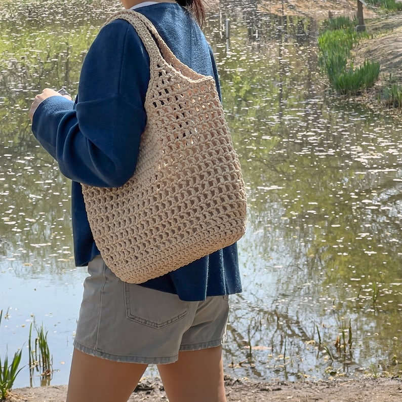 Puede incluir: Una persona con un su&eacute;ter azul y pantalones cortos de mezclilla lleva un bolso tote grande de crochet beige.