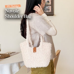 May include: DIY Package Nuvole Shoulder Bag. A white fluffy shoulder bag with a brown leather strap and buckle. The bag is being worn by a person.