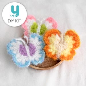 May include: Three crocheted butterfly-shaped bath scrubbers in a variety of colours, including purple, blue, green, pink, orange, and yellow. The scrubbers are on a wooden plate.