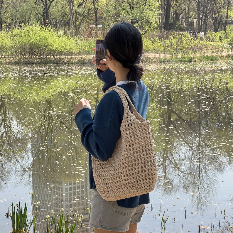 Puede incluir: Una persona con un su&eacute;ter azul y pantalones cortos de mezclilla sostiene un tel&eacute;fono inteligente y una bolsa de mano de crochet beige.