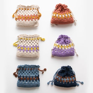 May include: Six crocheted drawstring bags in various colors and patterns. The bags are made with a granny square stitch and feature a contrasting color stripe around the middle. The bags are all the same size and shape.