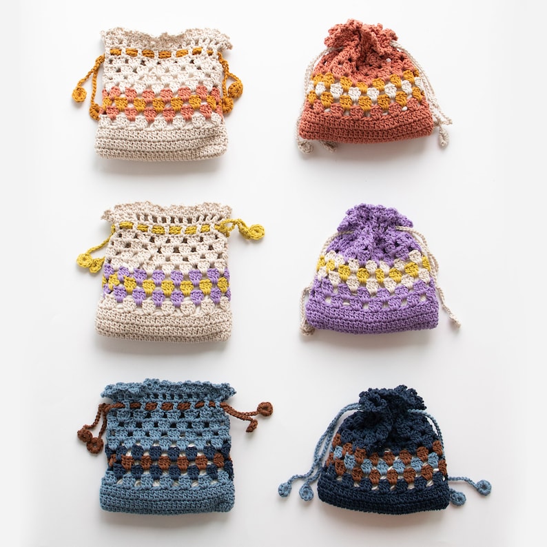 May include: Six crocheted drawstring bags in various colors and patterns. The bags are made with a granny square stitch and feature a contrasting color stripe around the middle. The bags are all the same size and shape.