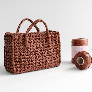 May include: A brown woven tote bag with two handles. Two spools of brown cord are in the background.
