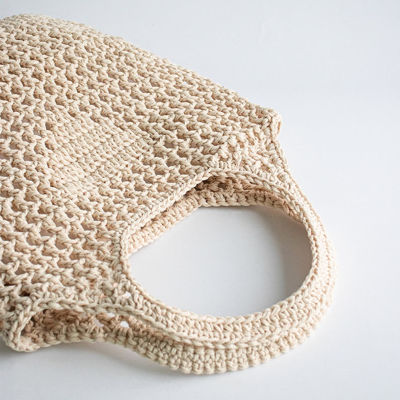 Puede incluir: Una bolsa de mano de crochet beige con un solo asa. La bolsa est&aacute; hecha de un tejido fino y abierto.