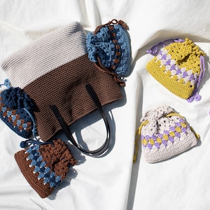 May include: A set of four crocheted bags in various colors and patterns. The bags are made with a combination of brown, white, blue, yellow, and purple yarn. The bags are all different sizes and shapes, and they are perfect for carrying small items.