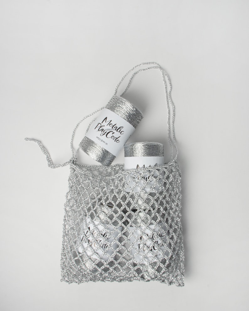 May include: A silver crochet bag containing two spools of silver metallic yarn. The yarn is labelled "Metallic Play Code".