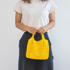 May include: A person holding a yellow crocheted tote bag. The bag has a square grid pattern.