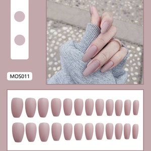 May include: A set of 24 nude-colored, coffin-shaped false nails. The nails are arranged in two rows of 12. MOS011