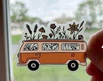 May include: A sticker of a vintage orange van with flowers growing out of the roof. The van has white trim and windows. The flowers are a variety of colors, including pink, purple, yellow, and green.