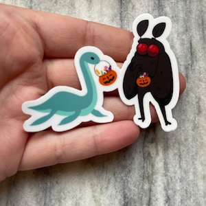 May include: Two Halloween-themed stickers featuring a blue and green plesiosaur and a black moth, both holding orange pumpkin pails filled with candy.