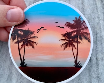 Könnte beinhalten: Ein runder Aufkleber mit einer Sonnenuntergangsszene, die zwei Palmen zeigt, die sich vor einem rosa und orangefarbenen Himmel abzeichnen. Der Himmel ist ein Farbverlauf von blau, rosa und orange, mit ein paar Vögeln, die am Himmel fliegen. Die Palmen befinden sich im Vordergrund, mit einem Strand im Hintergrund.