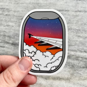 Puede incluir: Una pegatina de una ventana de avión con vista a una puesta de sol sobre las nubes. El cielo es un degradado de morado, rosa y naranja. Las nubes son blancas y esponjosas.