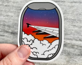 May include: A sticker of an airplane window with a view of a sunset over clouds. The sky is a gradient of purple, pink, and orange. The clouds are white and fluffy.