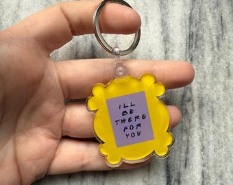 May include: Yellow plastic keychain shaped like a picture frame with the words "I'll be there for you" in black text on a purple background.