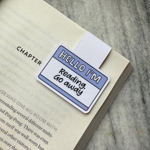 Könnte beinhalten: Ein blaues und weißes Lesezeichen mit dem Text "Hello I'm Reading. Go away." darauf gedruckt.