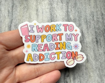 May include: A colorful sticker with the text "I work to support my reading addiction" with a book and glasses illustration.