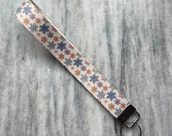 May include: A white key chain with a floral pattern and a silver key ring. The flowers are in shades of blue, pink, orange, and yellow.