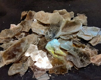 May include: A pile of iridescent mica flakes in shades of brown, green, and blue. The flakes are translucent and have a shimmering effect.