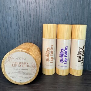 May include: Three brown sugar, coconut cream, and cocoa lip balms in bamboo tubes with the text "Buttery Lip Balm" and "Moisturizing Lip Balm". A brown bamboo jar with the text "Smokers Lip Scrub" and "Exfoliate + Soften Lips".