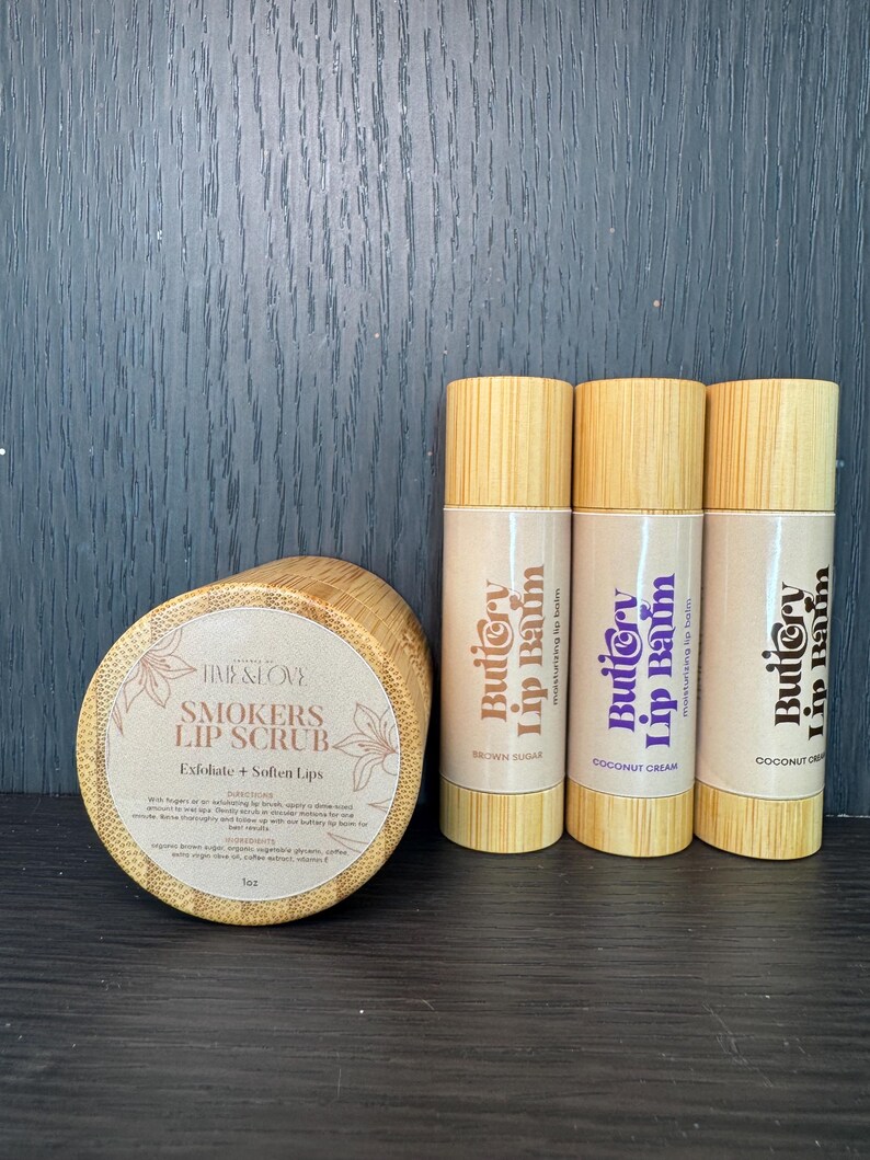 Puede incluir: Un conjunto de tres b&aacute;lsamos labiales en tubos de madera con el texto "Buttery Lip Balm" y los sabores "Brown Sugar", "Coconut Cream" y "Coconut Cream".  Tambi&eacute;n se muestra un tarro de exfoliante labial con el texto "Smokers Lip Scrub" y las palabras "Exfoliate + Soften Lips".