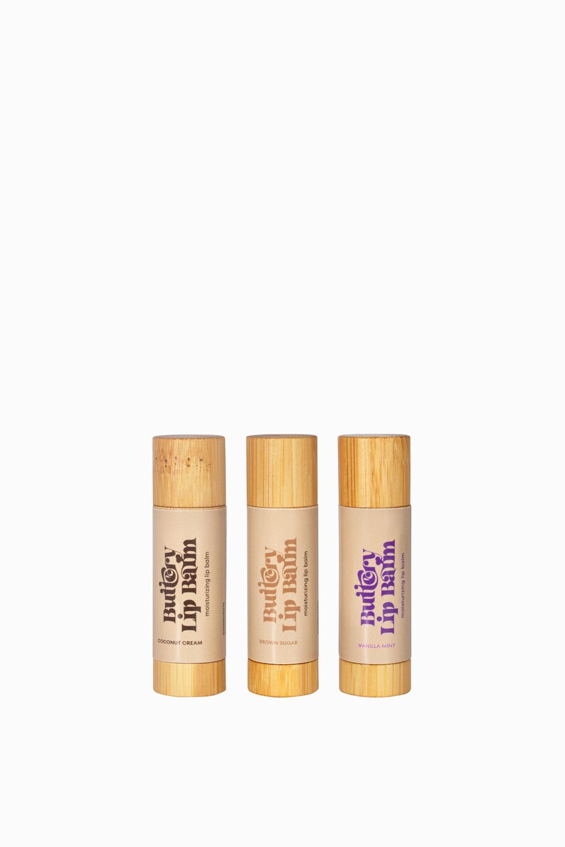 May include: Three wooden lip balm tubes with a purple and brown label that reads "Buttery Lip Balm" and a flavour name below. The flavours are Coconut Cream, Brown Sugar, and Vanilla Mint.