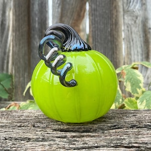 May include: A lime green glass pumpkin with a black and silver swirled stem.