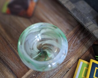 May include: A small, clear glass bowl with a swirling green and white pattern. The bowl is sitting on a wooden surface.