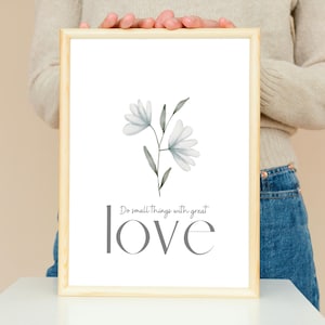 May include: A framed print with a watercolor illustration of a white flower with green leaves. The text "Do small things with great love" is printed below the flower.