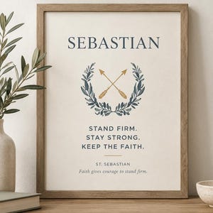 以下が含まれることがあります： SEBASTIANという名前がダークブルーの文字で記された額装されたウォールアートプリント。ダークブルーの月桂樹の冠の中に2本の金色の矢が交差したグラフィックが描かれています。その下にはSTAND FIRM. STAY STRONG. KEEP THE FAITH. ST. SEBASTIAN.というテキストがあります。