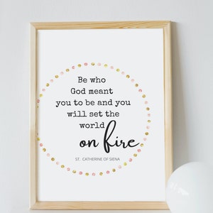 Puede incluir: Una impresión enmarcada con una cita de Santa Catalina de Siena: "Sé quien Dios quiso que fueras y encenderás el mundo." La cita está rodeada de un círculo de puntos rosas y dorados.