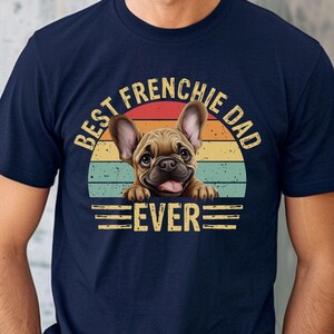 May include: A navy blue t-shirt with a vintage-style graphic of a French bulldog peeking over a sunset. The text reads "Best Frenchie Dad Ever".