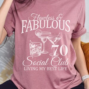 May include: Mauve t-shirt with white text and cocktail graphics. The text reads "Flawless & Fabulous 70 Social Club Living My Best Life". Features a margarita, martini, and old fashioned cocktail illustration.