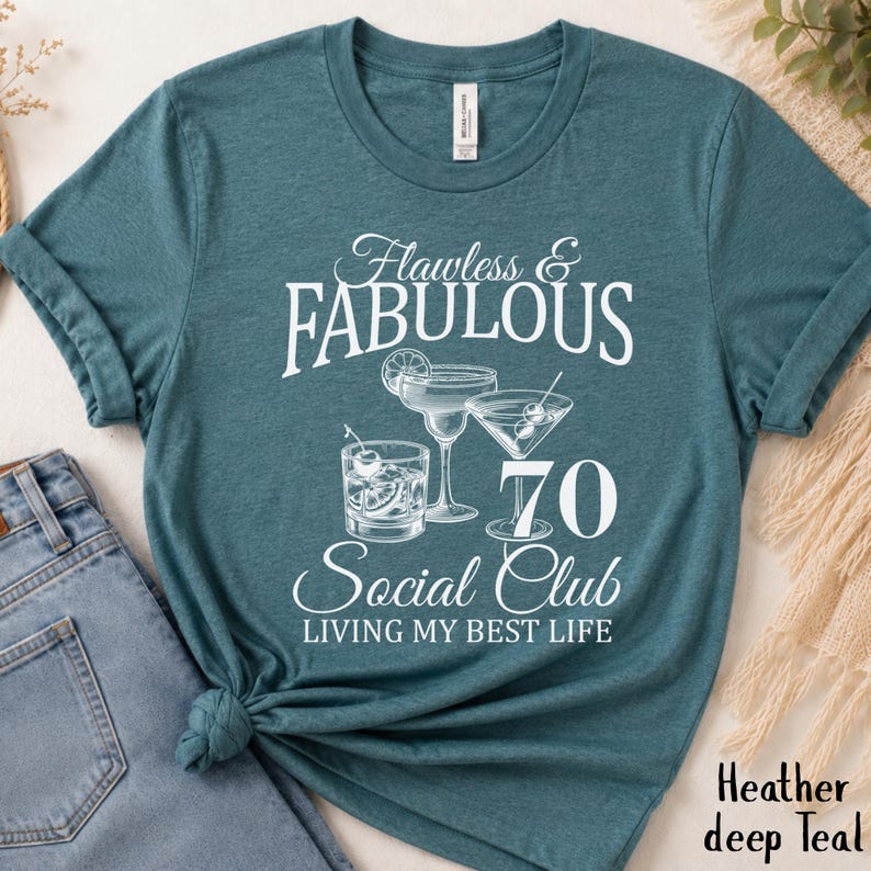 May include: Teal t-shirt with the text "Flawless & Fabulous 70 Social Club Living My Best Life". The shirt features illustrations of cocktails. The shirt is made of a soft material.