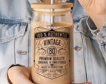 May include: A glass jar with a bamboo lid and a metal straw. The jar has a brown liquid inside and a black and white label that reads "100% Authentic Vintage 80 Premium Quality Original & Unrestored Aged to Perfection 1945".