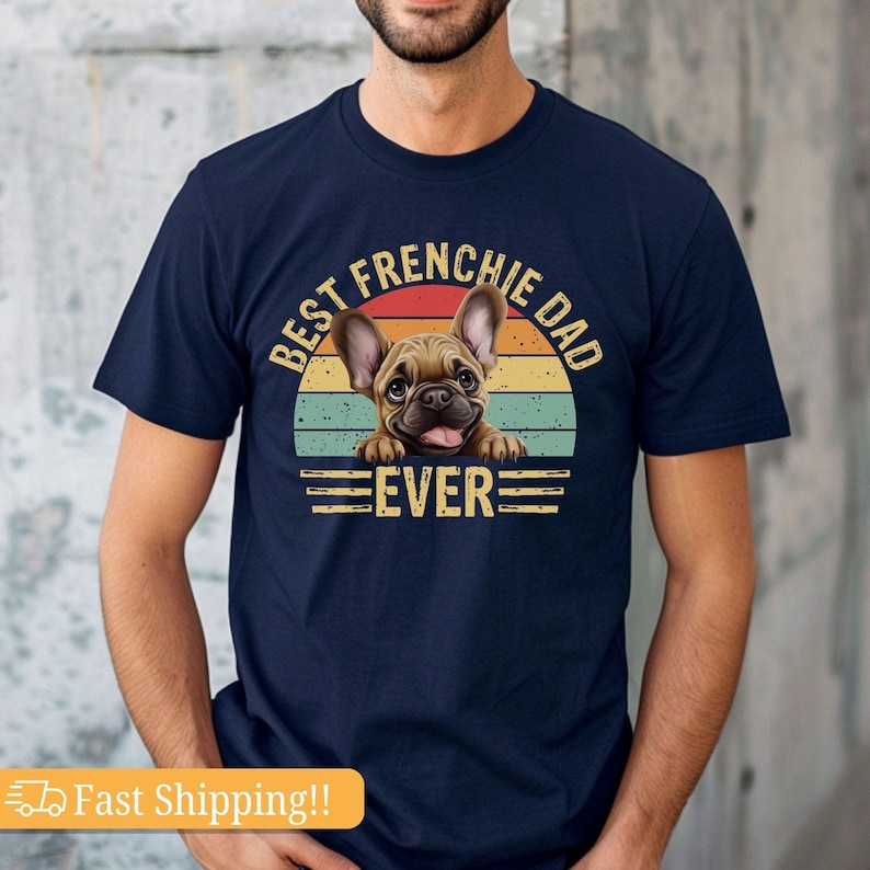 May include: A navy blue t-shirt with a vintage-style graphic of a French bulldog peeking over a sunset. The text reads "Best Frenchie Dad Ever".