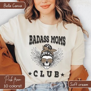 May include: A white t-shirt with the text "Badass Moms Club" in black with a skull wearing sunglasses and a leopard print bandana. The skull has angel wings.